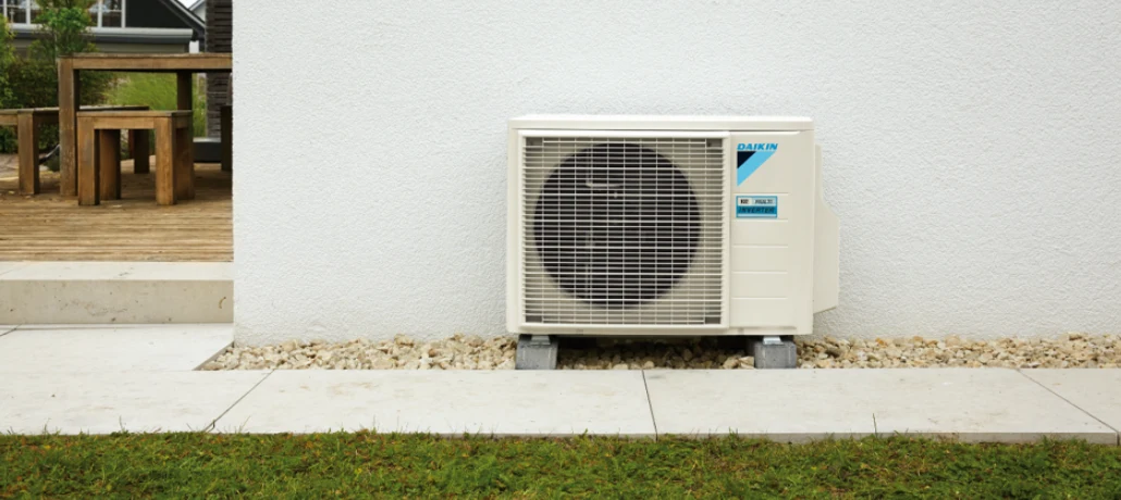 Groupe extérieur multisplit Daikin Sensira MXF-B posé sur plots contre un mur blanc, à côté d'une terrasse